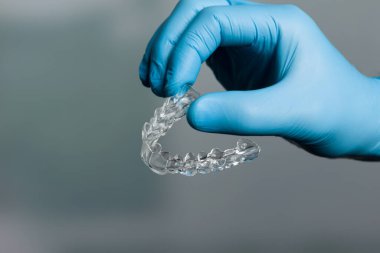 Diş hekimi mavi eldivenlerle dişçi odasının önünde şeffaf, çıkarılabilir bir sıralayıcı sunuyor.