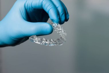 Diş hekimi mavi eldivenlerle dişçi odasının önünde şeffaf, çıkarılabilir bir sıralayıcı sunuyor.