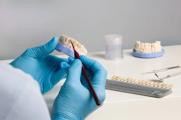 close-up of dental technician doing some painting work on tooth crown in dental laboratory