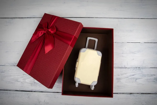Výlet jako dárek. červená dárková krabička s miniaturním cestovním kufříkem — Stock fotografie