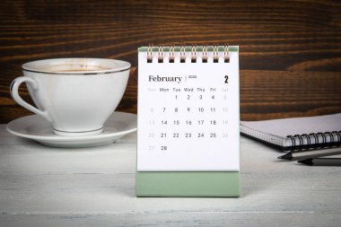 2022 Şubat. Masa takvimi, kahve fincanı ve ofis malzemeleri masanın üstünde.