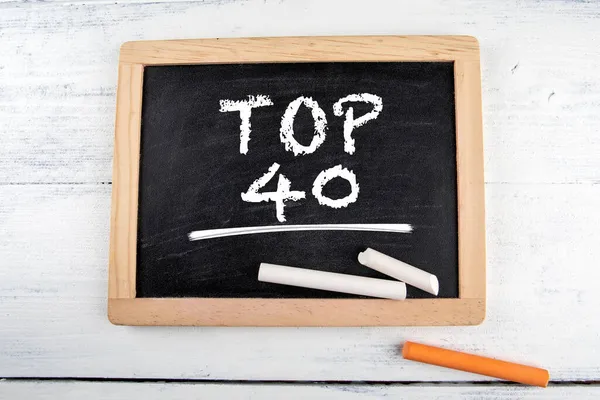 Top 40. pizarra de tiza negra con piezas de tiza en una mesa blanca — Foto de Stock