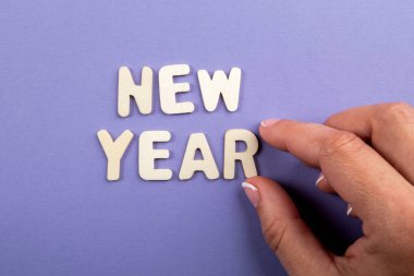 Yeni yıl. Alfabenin beyaz harfleri ve mor arka planda bir kadın eli.