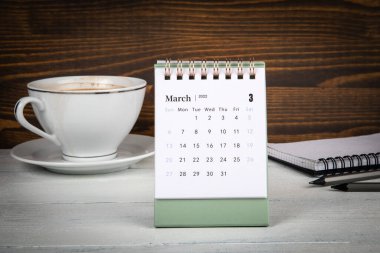 Mart 2022. Masa takvimi, kahve fincanı ve ofis malzemeleri masanın üstünde.
