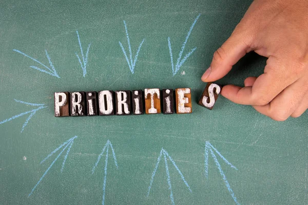 Prioridades. Palabra de letras de madera y una mano de hombre en una pizarra verde —  Fotos de Stock