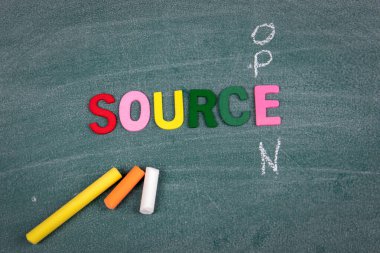 Açık Kaynak. Renkli ahşap harfler ve yeşil tahtadaki tebeşir parçaları.