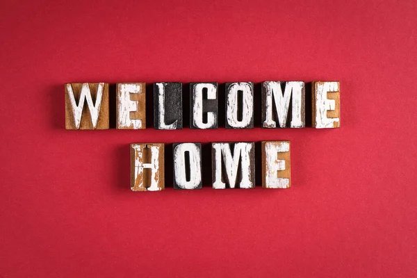 Vítej doma. Slova z dřevěných písmen na pozadí červeného papíru — Stock fotografie