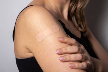 Woman shows the shoulder where vaccinated. Medical patch applied to the skin