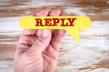 Reply. Yellow speech bubble in a mans hand on a wooden background