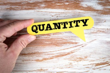 Quantity. Yellow speech bubble in a mans hand on a white wooden background