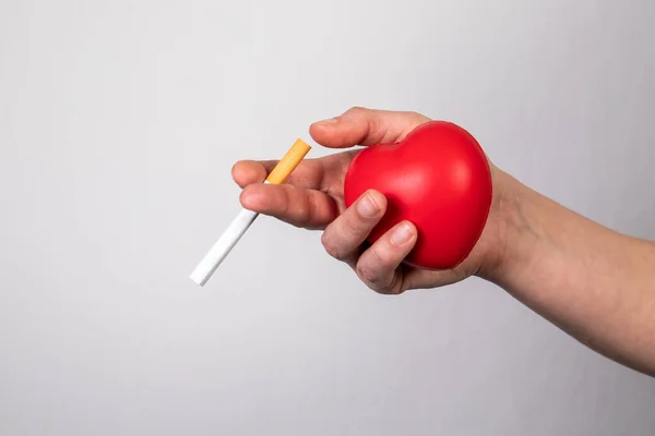 Γυναίκα κρατώντας ένα τσιγάρο και μια κόκκινη λαστιχένια καρδιά. κόψτε το κάπνισμα και την καρδιά έννοια της υγείας — Φωτογραφία Αρχείου