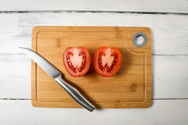 대나무 도마 위에 칼을 얹은 토마토를 반으로 자른 모습 — 스톡 사진