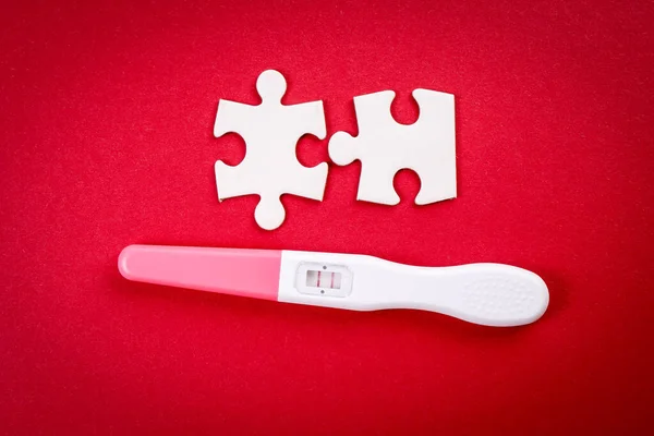 Positieve zwangerschapstest en witte puzzelstukjes op een rode achtergrond — Stockfoto