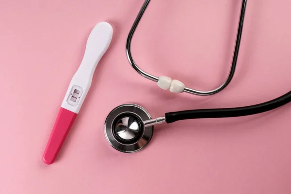Estetoscopio de los médicos y prueba de embarazo positiva sobre fondo rosa — Foto de Stock