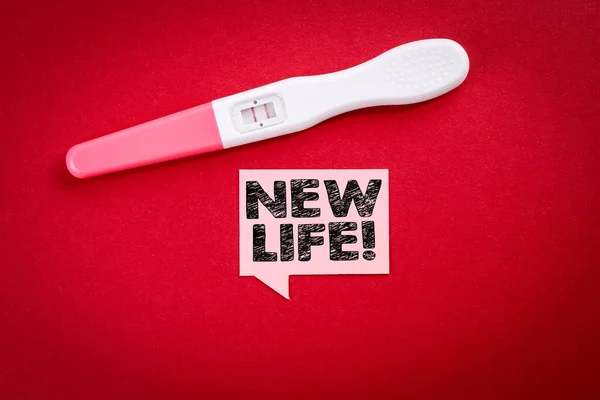 Uma vida nova. Bolha de fala com texto e teste de gravidez positivo em fundo vermelho — Fotografia de Stock