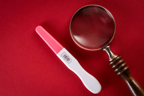 Teste de gravidez positivo e lupa em um fundo vermelho — Fotografia de Stock