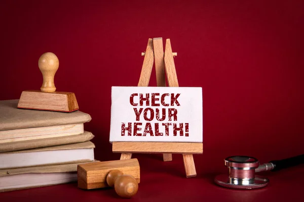 Verifica a tua saúde. Médicos estetoscópio e cavalete em miniatura com texto sobre um fundo vermelho — Fotografia de Stock