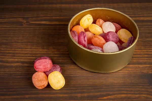 Colored candies in a pile and a metal box on a wooden background. Lollipops and sweets — Stock Photo, Image