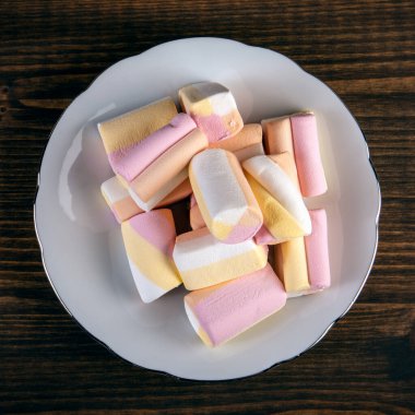 Ahşap bir arka planda beyaz bir tabakta renkli şekerlemeler yığını