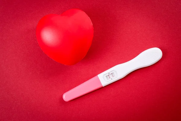 Teste de gravidez positivo e coração de borracha vermelha — Fotografia de Stock