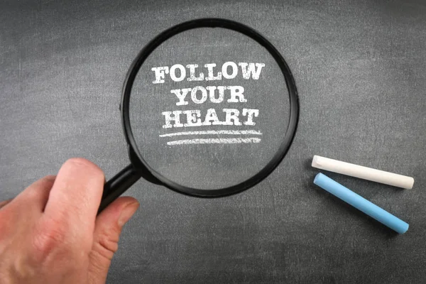 Följ ditt hjärta. Förstoringsglas och kritbitar på en mörk tavla — Stockfoto