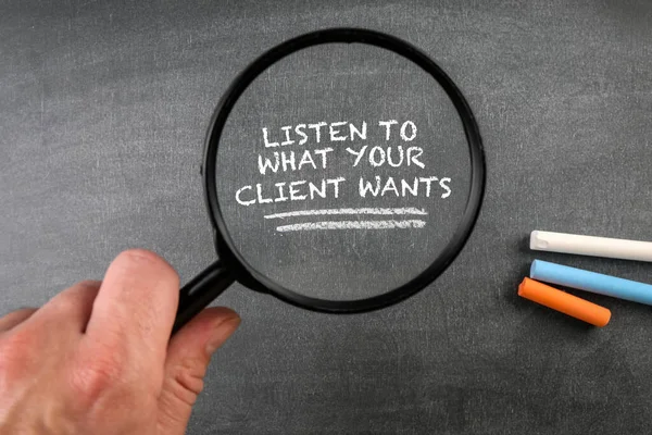 LISTEN TO WHAT YOUR CLIENT WANTS. Magnifying glass on a dark blackboard background