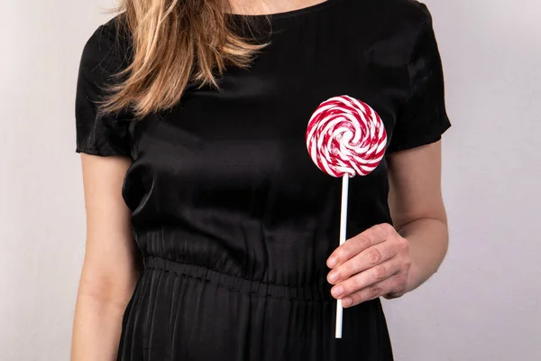 Candy on a stick in a woman s hand. Black dress and white background — Photo