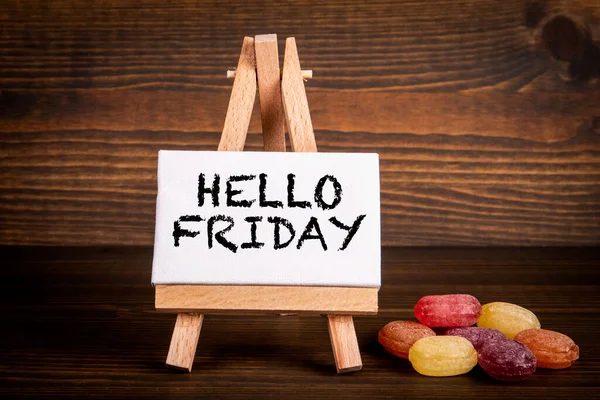 Hello Friday. Miniature easel and candy on a wooden background.