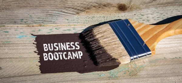 Business Bootcamp. Paint brush and brown paint on a wooden background.