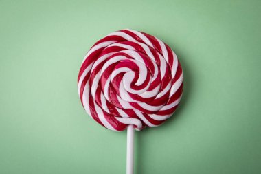 Brightly red candy, lollipop on a stick. Green background.