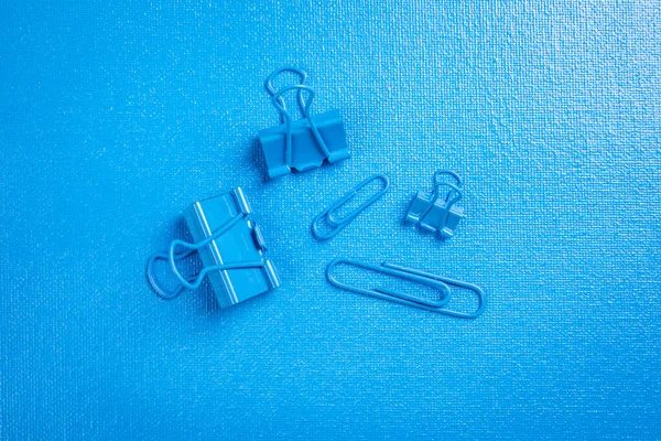 Paper clips and binder clips on a blue textured background.