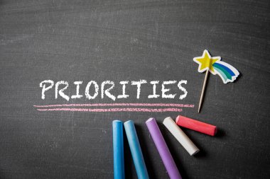 PRIORITIES. Text and colored pieces of chalk on a blackboard background.