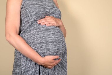 Pregnant woman in gray dress embracing her big abdomen. Maternity concept. Copy space.