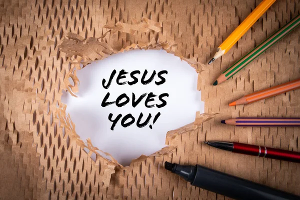 Jesus Loves You. Text and stationery on cardboard background.