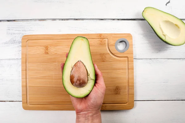 Avocado fruit in a womans hand. Bamboo cutting board in background.