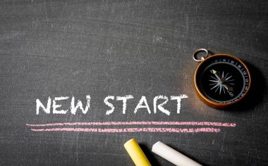 Yeni bir başlangıç. Tahta zemin üzerinde metin, pusula ve tebeşir parçaları.