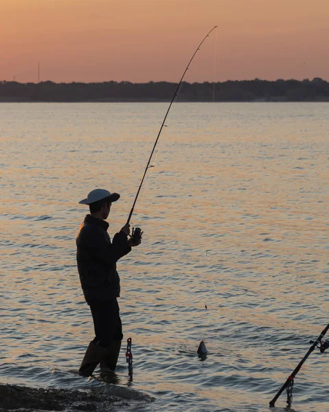 アメリカテキサス州ダラス近くのラボン湖でブーツと帽子の釣りを持つ正体不明のアジア人の男性の背面図 魚は水面のフックの上にあります — ストック写真