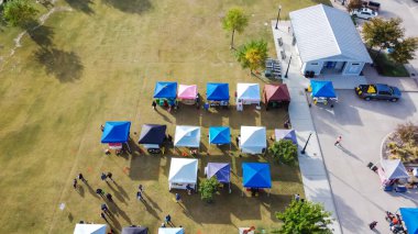 En renkli kabin, Amerika 'da Coppell, Teksas şehir merkezindeki şehir meydanındaki çimenli çimlerde alışveriş yapan meşgul insanlarla birlikte tuvaletin yanındaki çiftçi pazarında duruyor. Taze meyve, yerel çiftlikten sebzeler.