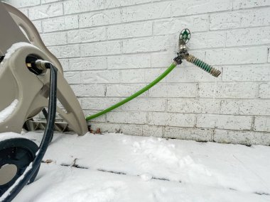 Kar hortumu kaplı mobil araba ve bahçe hortumu koruyucu bobininden akan uzun buz damlaları beyaz tuğla duvarda donmuş su musluğu. Dallas, Teksas 'ta soğuk hava nedeniyle buzlu musluk.