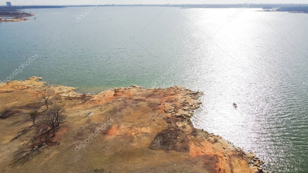 Small boat fishing near curved rocky shoreline with drop-offs, cliffs and bluffs at at Grapevine Lake, Texas, America. Aerial view lakeside park with picnic and camping areas.