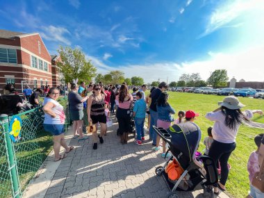 DUS, TX, US-APR 15, 2022: Çoklu etnik çeşitliliğe sahip çeşitli ailelerden oluşan kalabalık, çocuklarıyla birlikte yerel kilisenin çimen ilkbahar çayırında yumurta avını bekliyor. Amerika 'da geleneksel Paskalya kutlamaları.