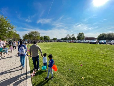 DOS, TX, US-APR 15, 2022: Renkli sepetleri olan çeşitli çoklu etnik çocuklar yerel kilisenin çim çayırında yumurta avını bekliyorlar. Amerika 'da geleneksel Paskalya kutlamaları.