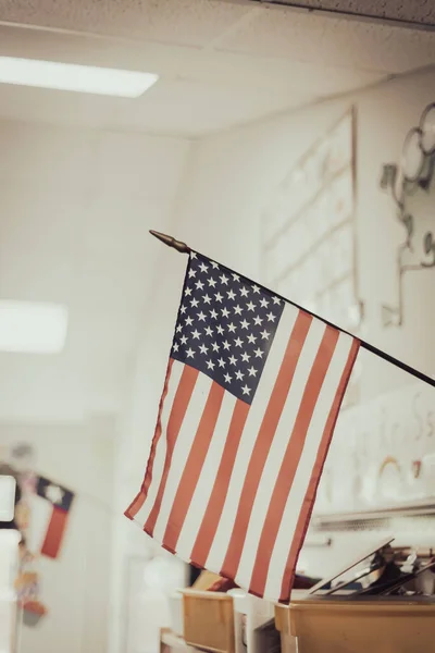 American flag with defocused Texas flag background in wall mouth flagpole in kindergarten classroom in public Texas elementary school. Patriotic and educational background