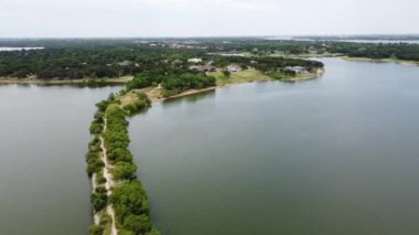Top view lush green hiking trail lead to the lakeside neighborhood with upscale two story house in Lakewood Village, Texas, USA. Long straight lakeside unpaved road path to horizontal line