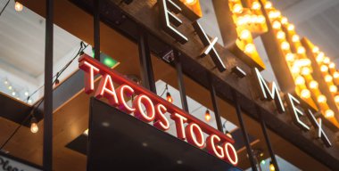 Panorama view Tex Mex restaurant welcome sign with LED Tacos to go text in Texas, America. Lookup view of large Taco take away text at modern airport eatery.