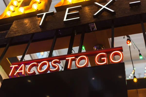 Colorful light bulb and red LED Tacos to go text at Tex Mex restaurant in Texas, America. Lookup view of large Taco take away text at modern airport restaurant.