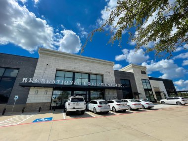 SOUTHLAKE, TX, US-AUG 28, 2022: Green oak leaves and wide angle view exterior entrance of REI Recreational Equipment, Inc store with parked cars in front under sunny cloud blue sky