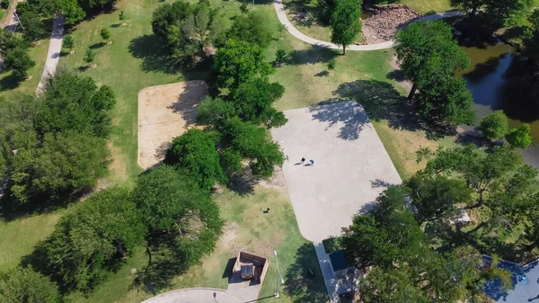 Basketball court in community park with people playing at midday summertime near Richardson, Texas, USA. Aerial view community recreational place with mature green trees, trails and pond