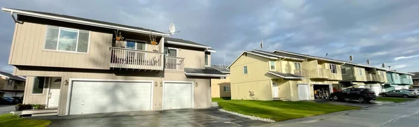 Panorama view two story duplex houses, two units in same building, share a common wall in Anchorage, Alaska. Multi-family home arranged side by side large concrete pathway curb appeal