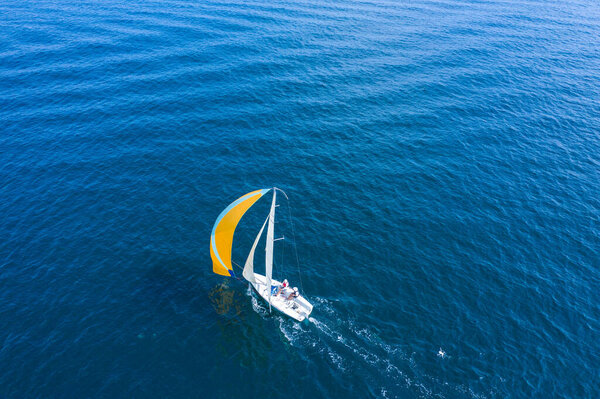 Летние каникулы на воде. Вид с воздуха на красивую белую парусную яхту с цветным парусом.